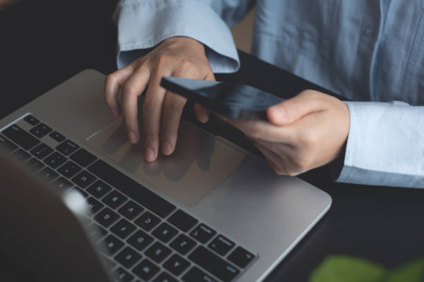 istock Business woman sitting at office table using mobile phone while online working on laptop computer at home office, business casual, telecommuting, working from home, close up 1728833597