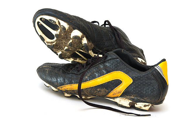 Muddy black and yellow football boots on a white background stock photo