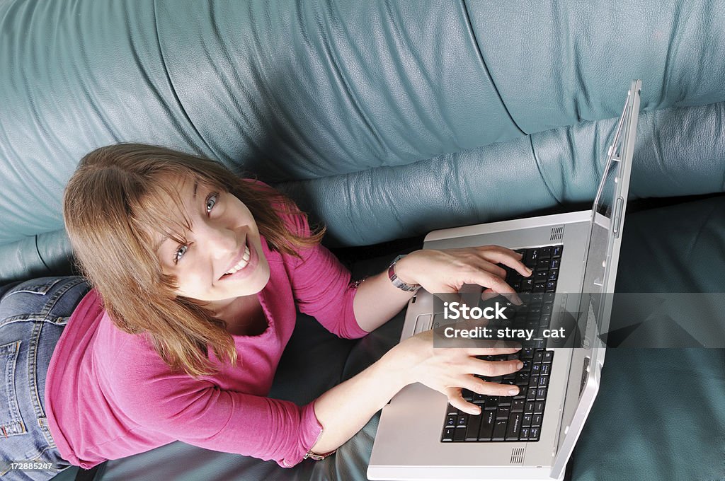 Laptop Smile A young woman uses a laptop while lying on a couch.Also available: 20-24 Years Stock Photo