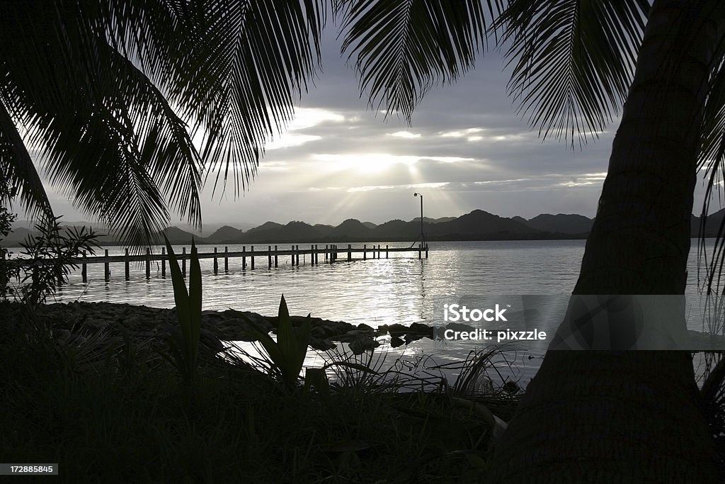 Belize Southern Lagoon Cloud Palm Pier "Sunset through clouds; pier at Manatee Lodge, Southern Lagoon, Belize." Back Lit Stock Photo