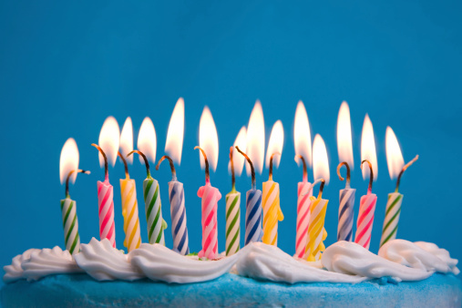 Close-up of flaming birthday candles on a cake against a blue backdrop.  Shallow DOF.