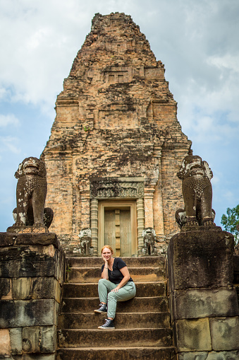 A captivating stock image capturing the adventurous spirit of a young red-haired woman as she explores the awe-inspiring ruins of Angkor Wat in Siem Reap, Cambodia. With a backpack slung over her shoulder, she immerses herself in the rich history and intricate architecture of this UNESCO World Heritage site.\n\nIn this photograph, the subject's sense of wonder and curiosity is palpable as she navigates the ancient temples, revealing the timeless allure of Angkor Wat. Her journey is a testament to the transformative power of travel and the exploration of new cultures and landscapes.\n\nThis image beautifully encapsulates the spirit of adventure and the indomitable curiosity of the modern traveler, making it an ideal asset for a wide range of creative projects that celebrate the joy of exploration and cultural discovery in one of the world's most iconic historical sites.
