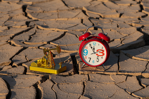 Model of a golden oil pump and a red alarm clock on cracked clay in the desert