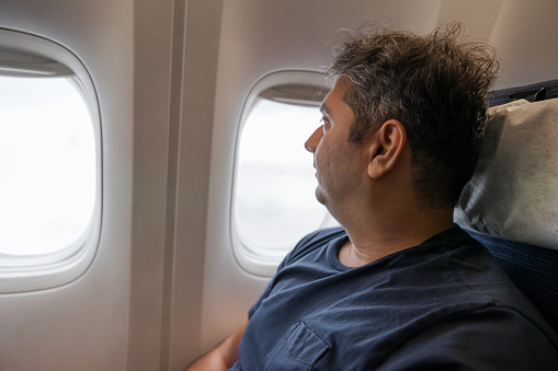 Indian man looking outside an aircraft window on a flight to Paris