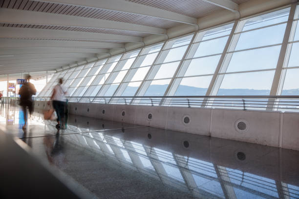 Motion blurred motion people walking with luggage at American airport. Abstract blurry passengers or tourist with bag, back view. Defocused traveler away at hallway terminal, morning lights backlit