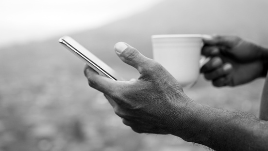 Person using smartphone. Hand of businessman checking phone while holding a cup of tea in black and white background.