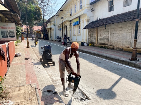 Mangalore, India - January 16 2023: A construction labourer drilling a hole in concrete on a street,