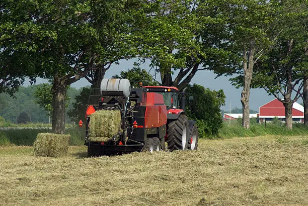 A farmer baling hay with a large square baler.