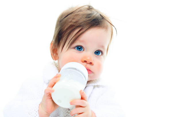 Baby drinking from milk bottle against white stock photo