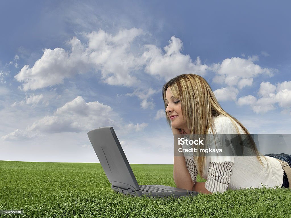 Happy Girl On Grass A happy young girl lying down on grass and using computer (laptop) with cloudy sky background. 20-29 Years Stock Photo