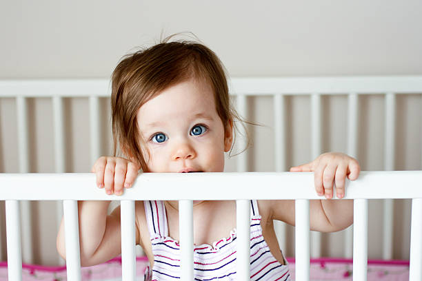 Sweet baby girl looking out over her crib rail stock photo