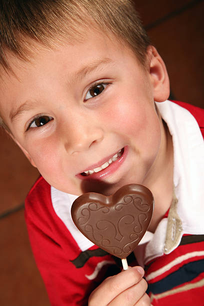 sorrindo linda criança comer pirulitos de chocolate em formato de coração - child valentines day candy eating - fotografias e filmes do acervo