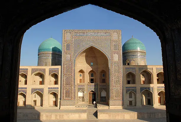 "view of the Amir alim Khan Madrasa (Madrasah) in Bukhara, Uzbekistan framed in the arch of a mosque"