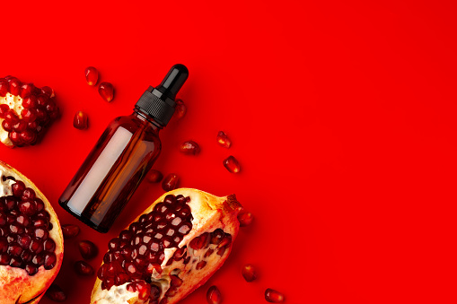 Cosmetic serum dropper bottle with pomegranate flavor on red background close up