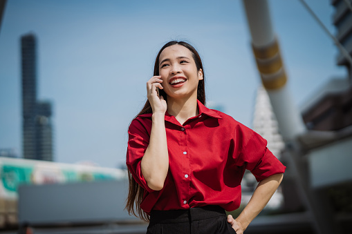 Young enthusiastic woman is talking on the phone and smiling in the urban city setting.