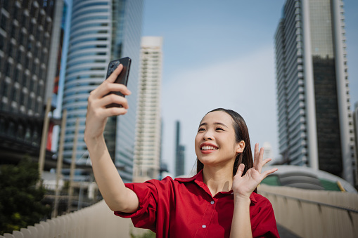 Young enthusiastic woman is having a video call and smiling in the urban city setting.
