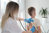 The doctor listens to the breathing of a little boy through a stethoscope. Pediatrician with stethoscope listens to the lungs of a child with bronchitis and cough