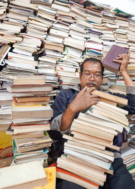 Lecturer reading a book in the university library, looking exhausted and tired from studying. Sleeping on stacks of books