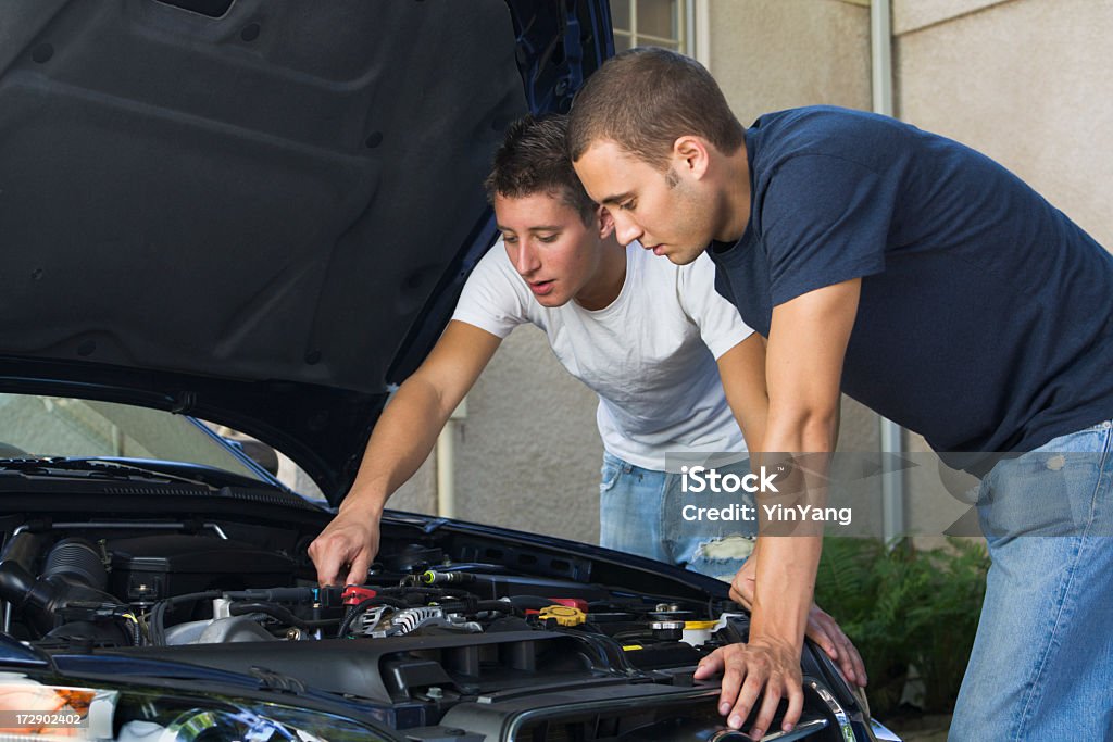 Car Repair and Engine Maintenance, Men Working Examining Under Hood Two young man working on the engine of a car, repairing or maintaining machinery under the hood. Car Stock Photo