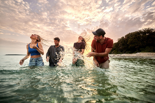 Young playful couples having fun during their summer vacation in sea at sunset. Copy space.