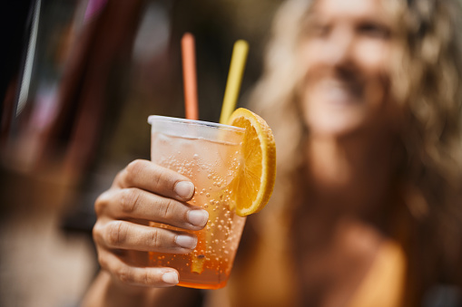 Close up of unrecognizable woman holding fresh orange juice in disposable cup.