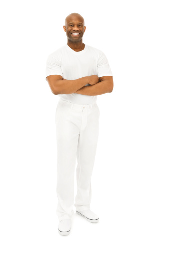 Photo of a bald African American man in white shirt, white pants and white shoes, standing with arms folded against a white backdrop.