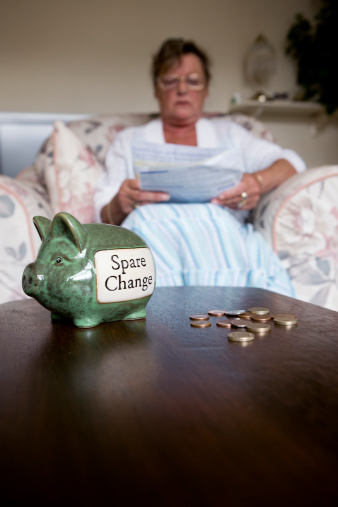 A senior woman checking her bill statements. Focus on the foreground piggy bank and coins.