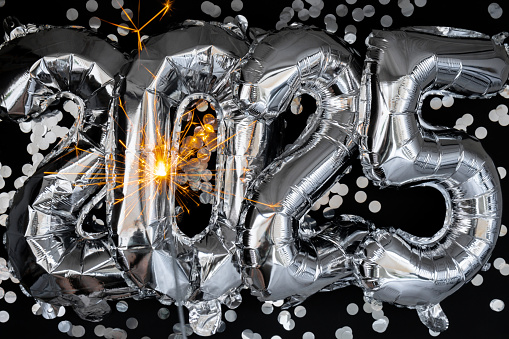 Happy new year 2025 metallic balloons with confetti and sparkler firework Bengal lights on dark black background. Greeting card silver foil balloons numbers Christmas holiday concept. Celebration party congratulation decoration