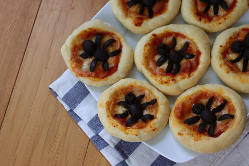 Halloween mini spider pizzas with black olives on plate on wooden table