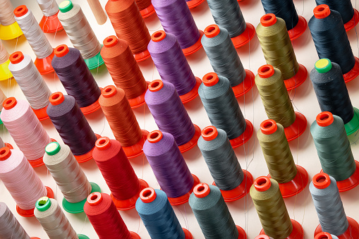 Row of multicolored thread spools at sewing factory close up