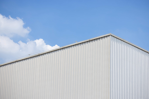 metal sheet factory warehouse against blue sky background. silver corrugated steel industrial roof.