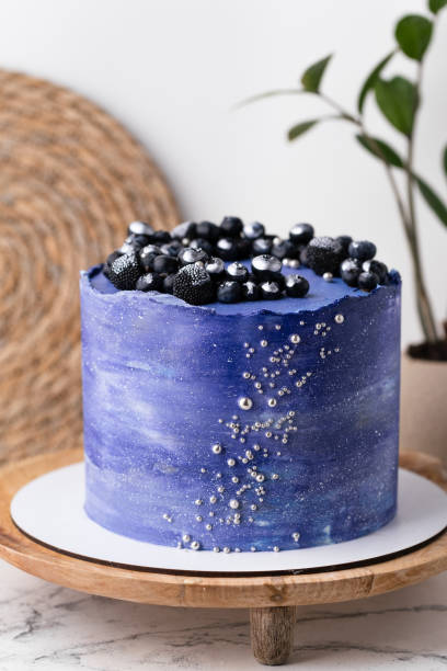 istock Birthday cake with blue cream cheese frosting decorated with blueberries covered with silver kandurin. Cosmic cake or space themed cake on the white background. 1729082179
