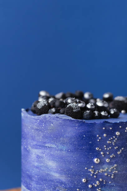 istock Birthday cake with blue cream cheese frosting decorated with blueberries covered with silver kandurin. Cosmic cake or space themed cake on blue background. 1729082249
