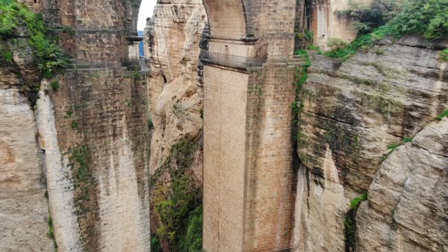 Aerial fly toward arch shot of tall medieval Puente Nuevo bridge and the chasm rift in Ronda, Andalusia, Spain
