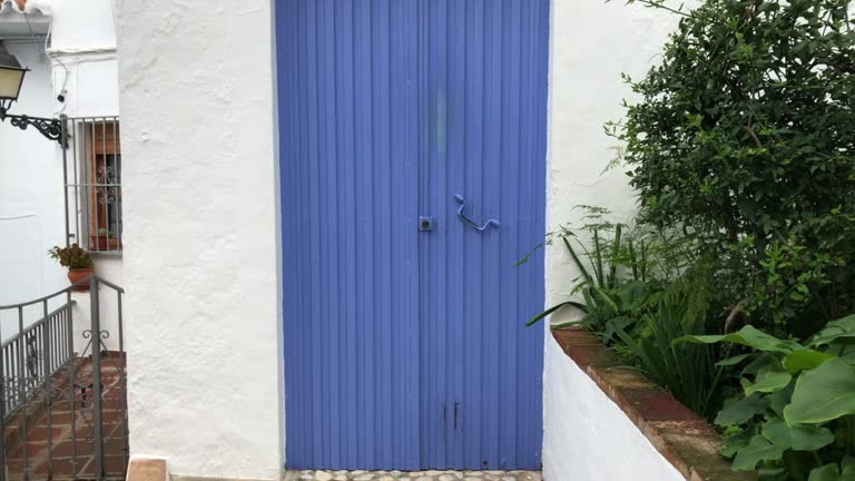 Dolly Out Shot of blue painted rusty metal door on white wall building in Frigiliana, Spain