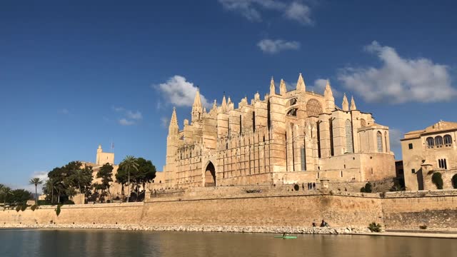 Orbital hyper lapse shot of sunlit Mallorca Cathedral in Palma, Spain. sunny day with clouds, pedestrians, tourist, and kayak
