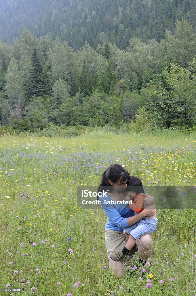 Mujer agarrando su hija en un prado flor equipada - Foto de stock de Abrazar libre de derechos