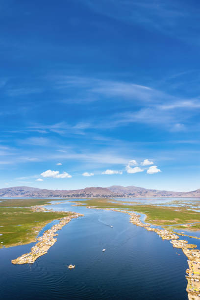 Llachon beach on the shores of Lake Titicaca, Peru, features calm waters, golden sand, and a distant mountainous landscape under a bright blue sky with fluffy clouds