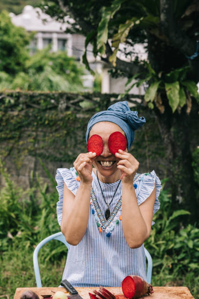 Portrait of Japanese woman's lightheartedness as she giggles while holding two melons in front of her eyes, turning her side hustle detox juice preparation into a fun\n\nMoui: モーウィ (赤毛瓜)\nChinese cucumber\nred gourd\nyellow cucumber\nOOITABI NO MI\npassion fruit