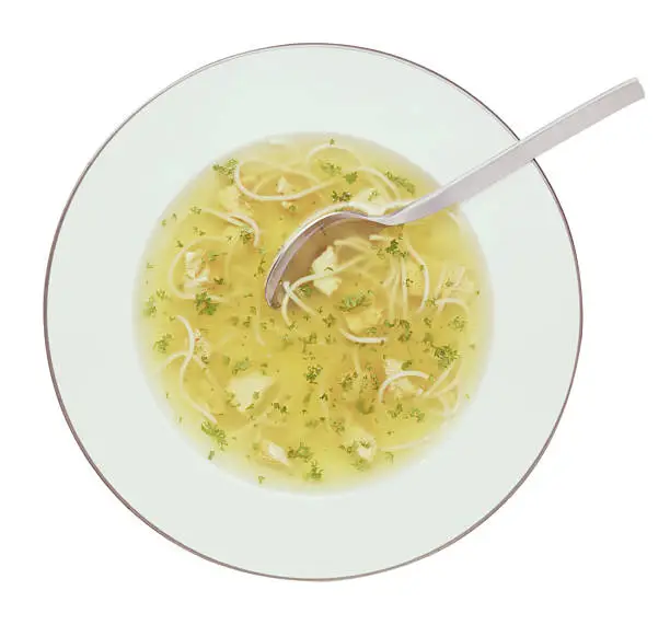 "clear chicken soup in a soup plate with vermicelli, parsley and smal pieces of white chicken meat"