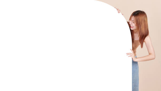 Young Asian woman is standing behind the white blank banner or empty copy space advertisement board on isolated background.