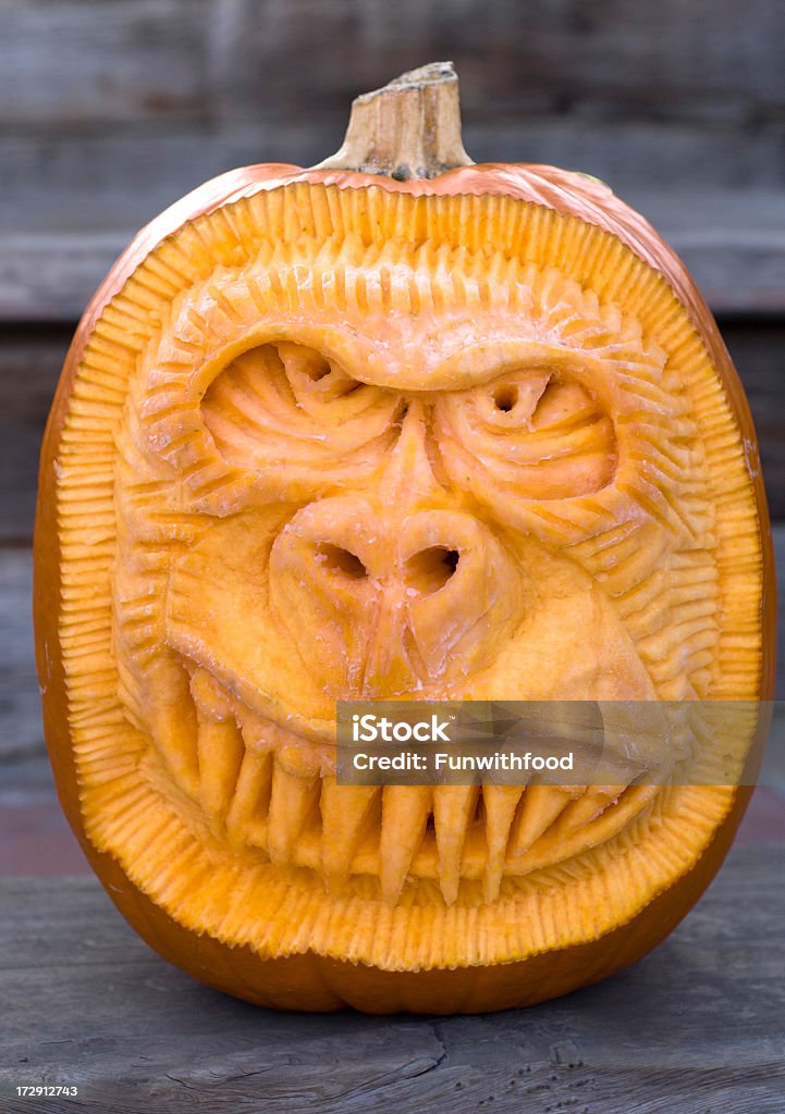 A carved Halloween Jack O'Lantern against wooden background Fresh spooky monkey pumpkin, carved Halloween jack o' lantern decoration on front porch. (SEE LIGHTBOXES BELOW for more atuumn vegetables, holiday backgrounds...) Carving - Craft Product Stock Photo