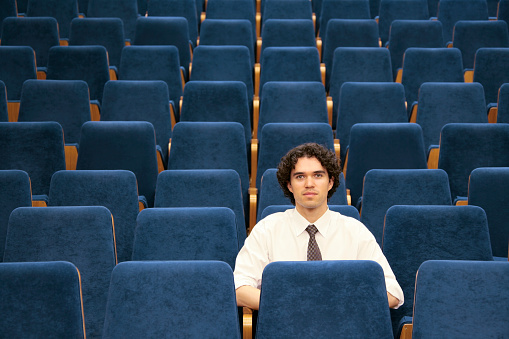 Young businessman sitting in an empty conference hall (or movie/theatre).