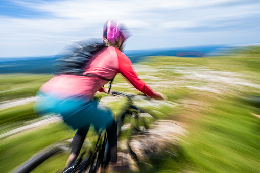 Woman riding electric bike fast on mountain road, blurred motion view