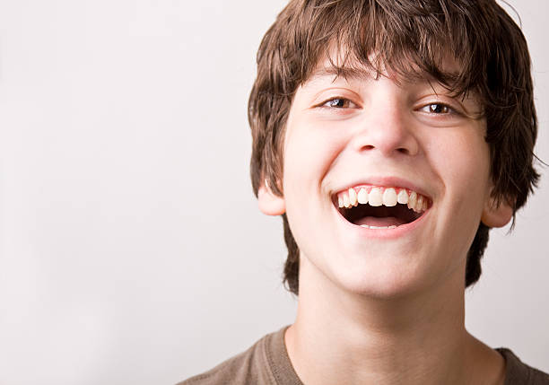 laughing boy "A close-up shot of a boy laughing, isolated on light gray." happy young teens stock pictures, royalty-free photos & images