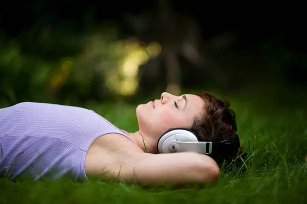 Young attractive girl listening to headphones lying on grass