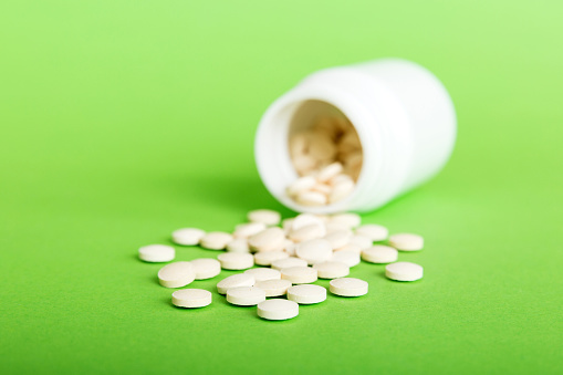 Medicine bottle and white pills spilled on a light background. Medicines and prescription pills flat lay background. White medical pills and tablets spilling out of a drug bottle.