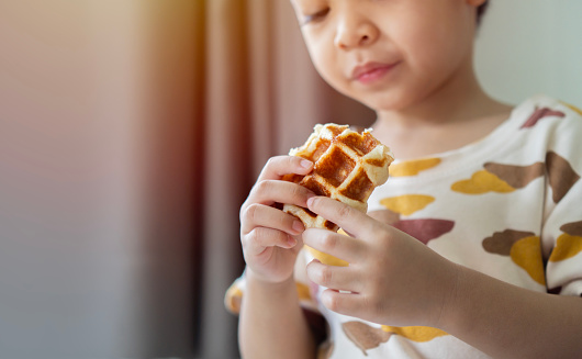 Shot of happy little preschool boy holding fresh baked waffle at home in the morning. Sweet sugar belgian waffles, copy space.
