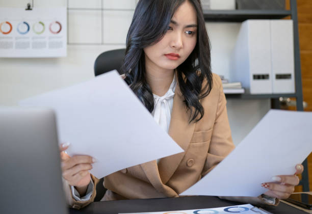 istock Pretty Asian woman sitting in the office working on data, charts and documents on the table in business workspace. Portrait of young concentrated business woman reading documents. 1729174929