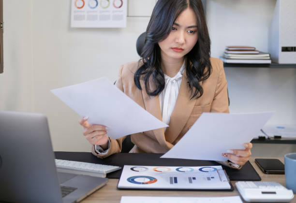 istock Young concentrated businesswoman reading documents and sitting at table in office. Serious focused businesswoman holding papers preparing report analyzing work results. 1729175529